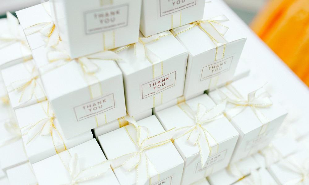 A top-down perspective of a pile of white wedding favor boxes tied with golden ribbons and thank-you messages.