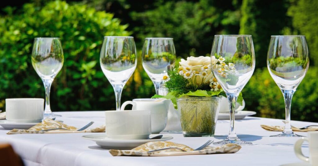 Five clear wine glasses spread out among decorative napkins and a floral centerpiece on an outdoor table.