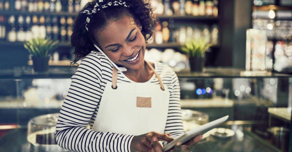 A restaurant hostess or manager taking reservations on a tablet. She balances a cell phone on her shoulder.