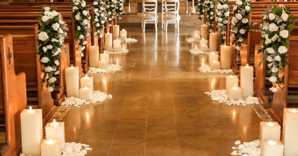 The aisle of a wedding ceremony. The aisle is lined on both sides with green and white flowers and pillar candles.