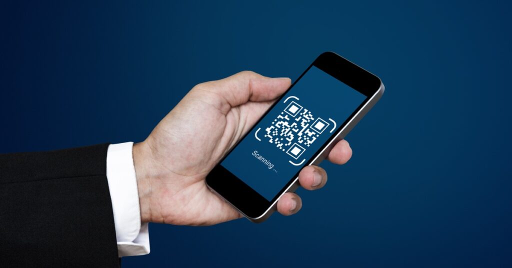 A close-up of a person in a suit holding a black smartphone with a QR code on the screen, set against a blue background.