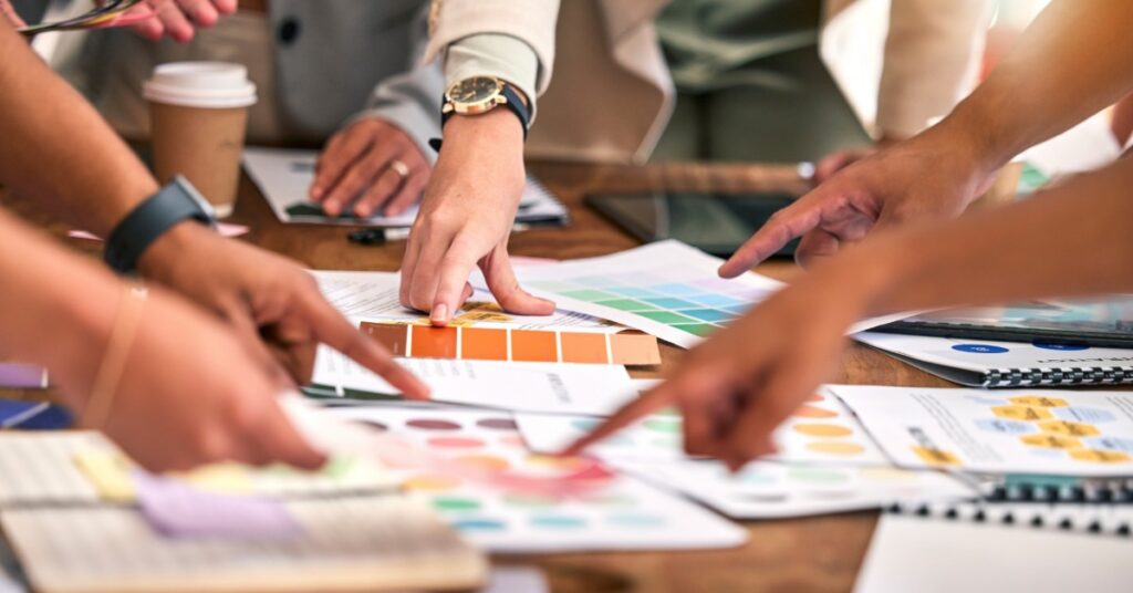 Team members point at color swatches and design charts on a table, collaborating on branding materials.